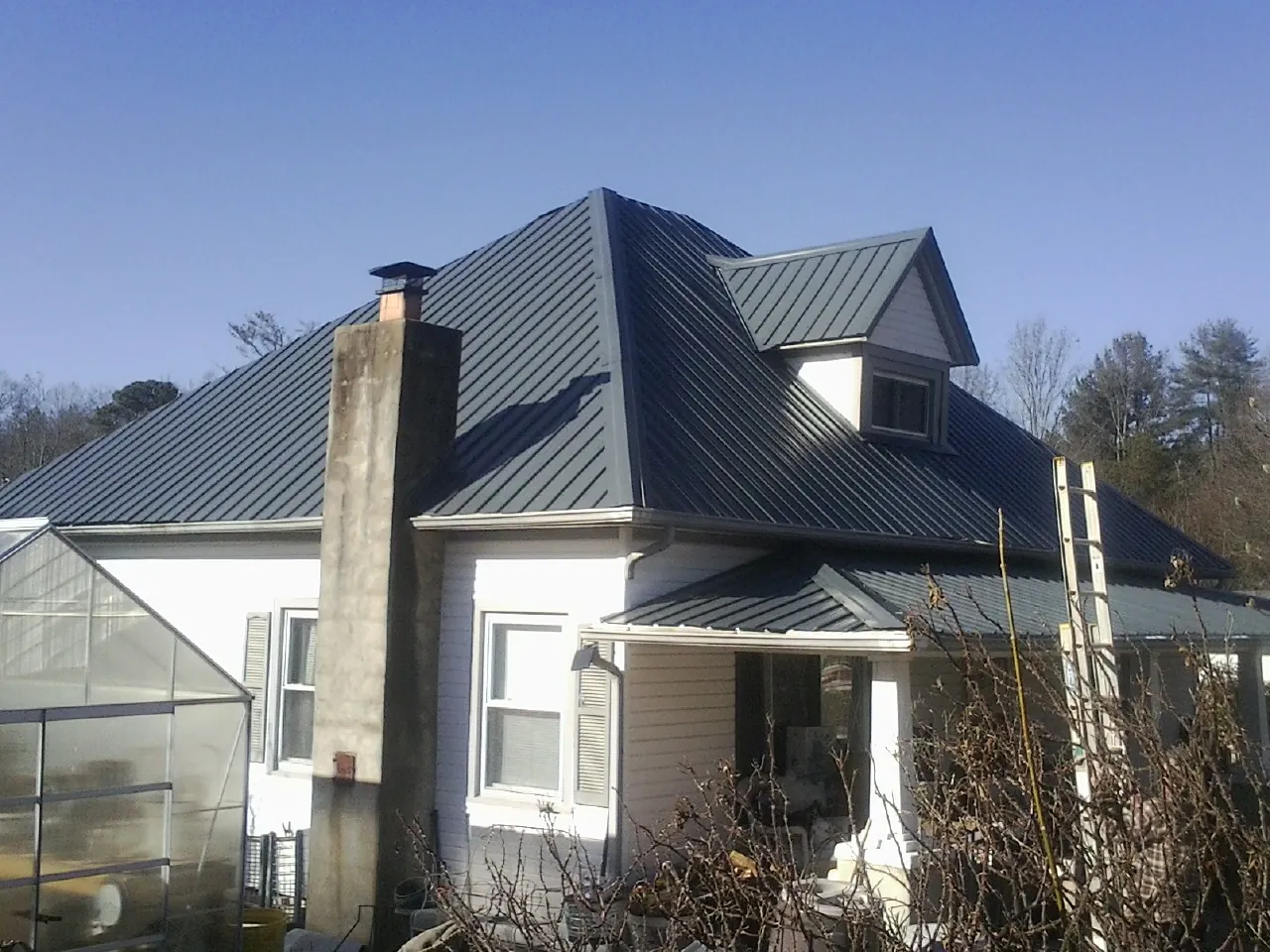 Dark blue standing seam metal roof on a white farmhouse with dormer — Slate & Tile Roof Repair by Roofing Brothers in Chesterland