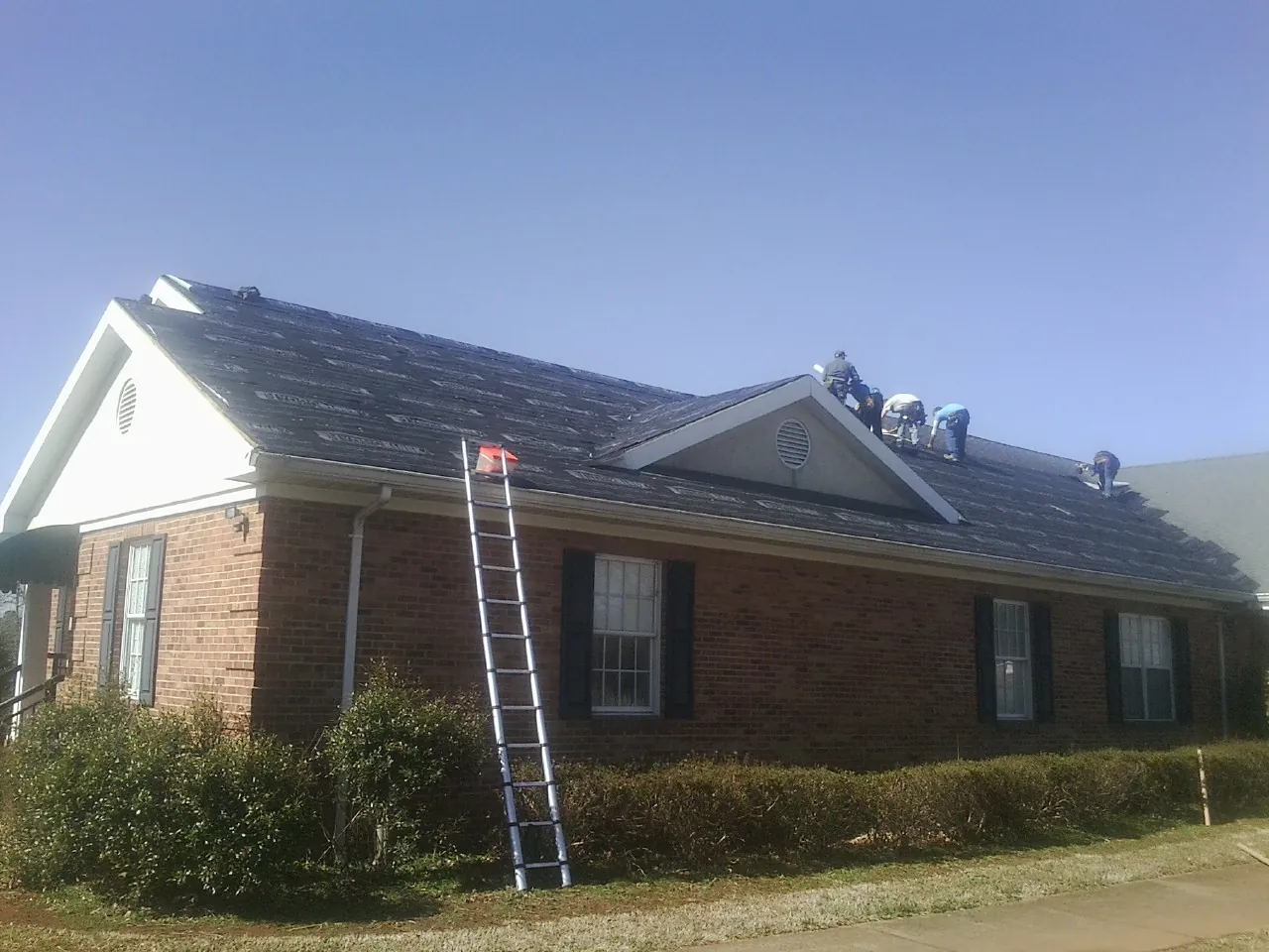 Crew tearing shingles off a brick ranch roof with a ladder set — Metal Roof Repair work by our crew in Chesterland