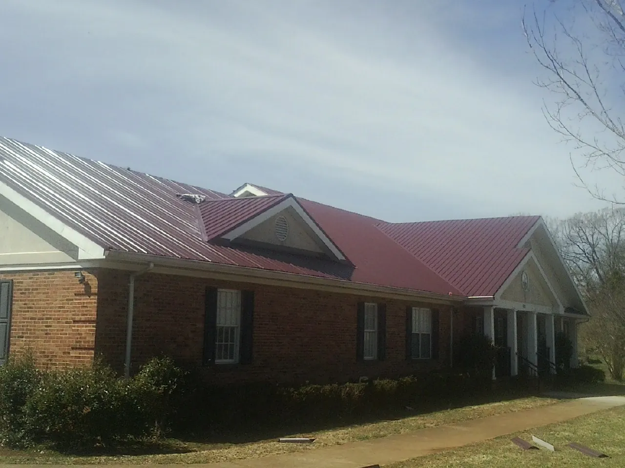 Red metal roof with gabled entries on a long brick building, from a Hail Damage Roof Repair job in Chesterland