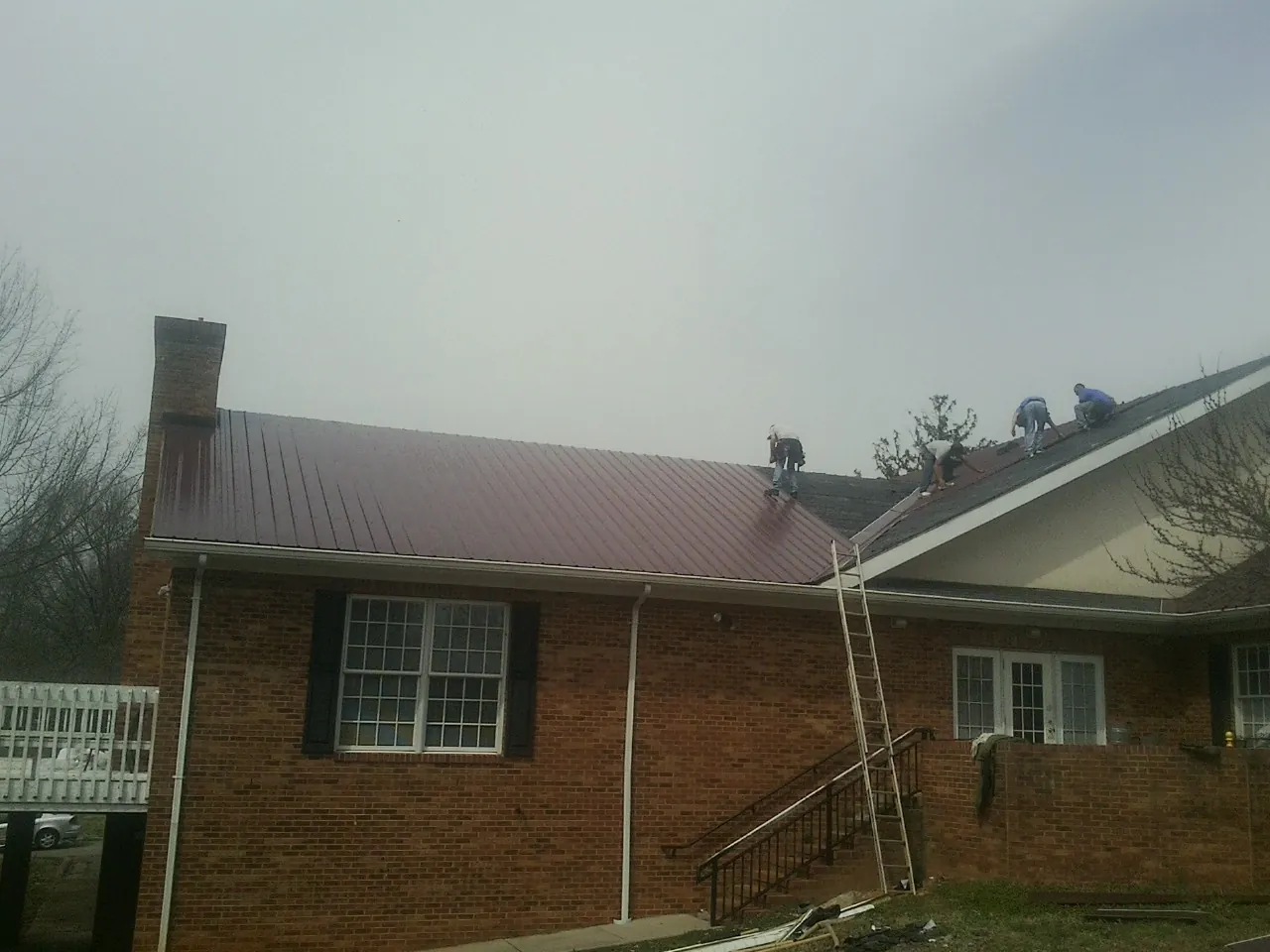 Crew setting red metal roofing panels on a brick home in Chesterland