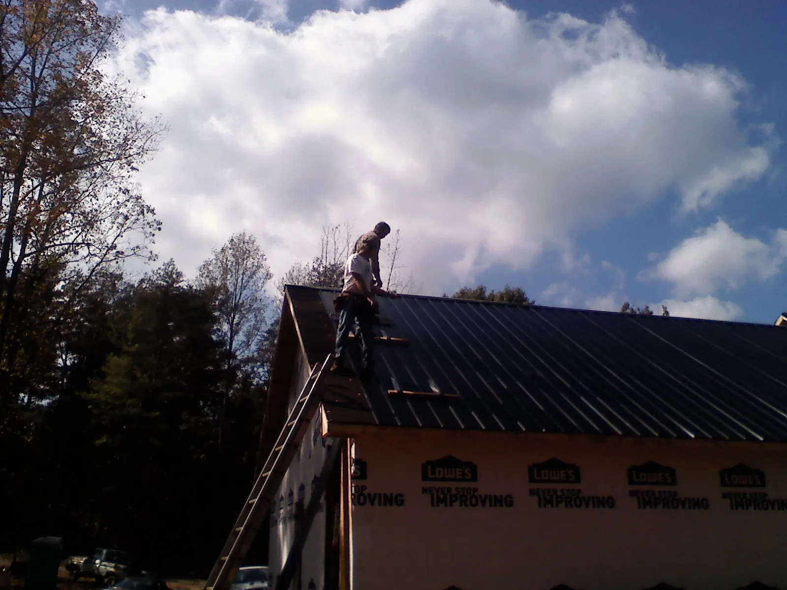 Roofer fastening dark metal panels high against a cloudy sky, from a Roof Inspection job in Chesterland
