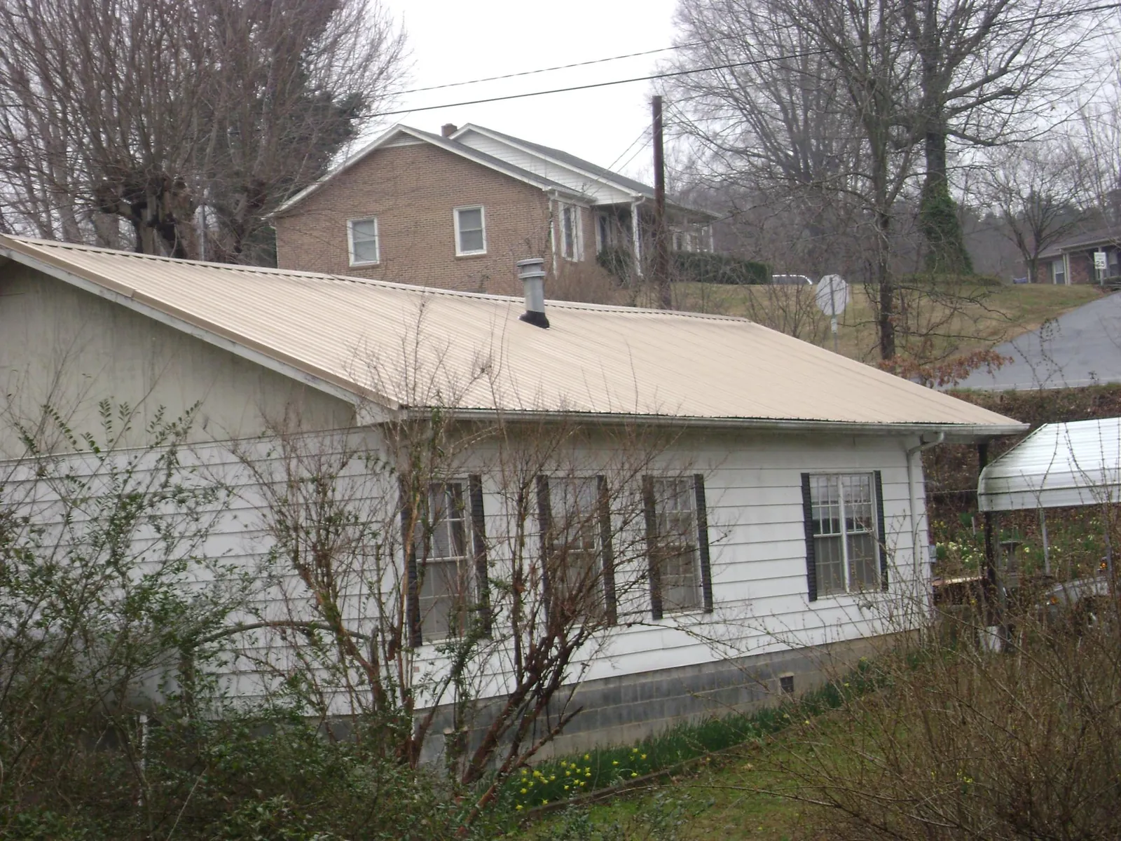 Tan metal roof on a white sided house set into a hillside — Commercial Roofing by Roofing Brothers in Chesterland